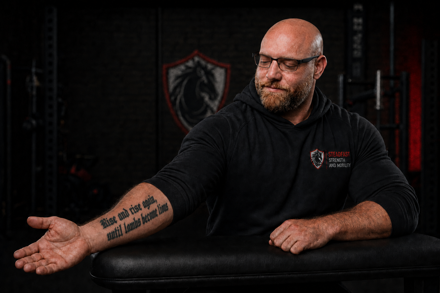 Steadfast Strength and Mobility founder looking thoughtfully at the quote tattooed on the inner part of his right forearm inside the gym.