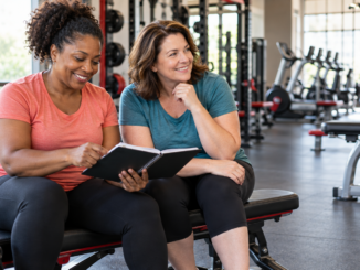 Two women reviewing a training notebook together in a welcoming gym.