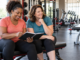 Two women reviewing a training notebook together in a welcoming gym.