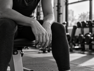 Black and white image of a person resting on a gym bench between sets.